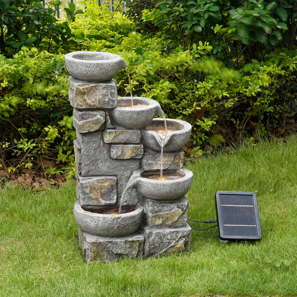 Tiered stone water fountain with a solar panel next to it in a green grassy garden area. 