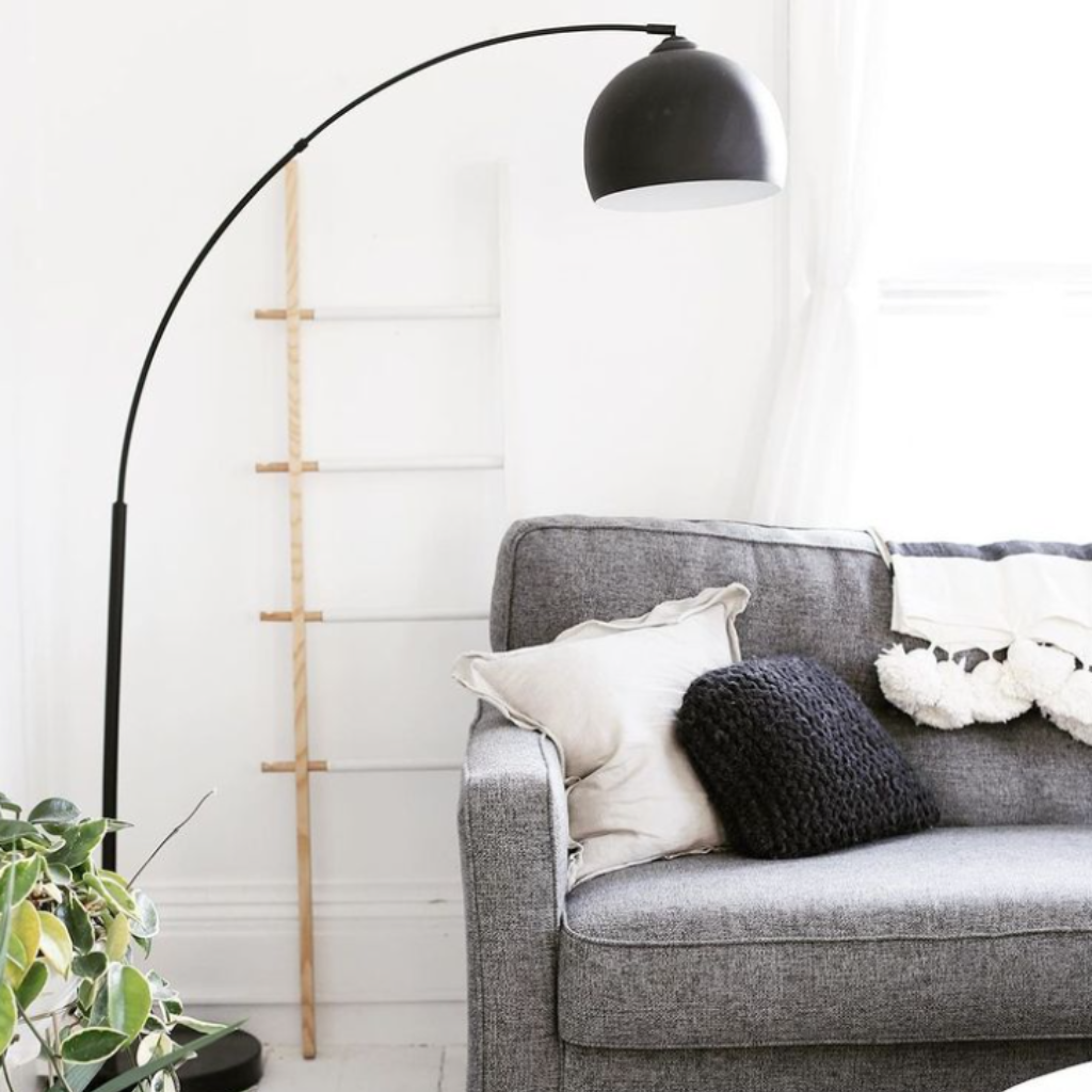 Black teamson floor lamp sits in the corner of a living room next to a grey sofa. 